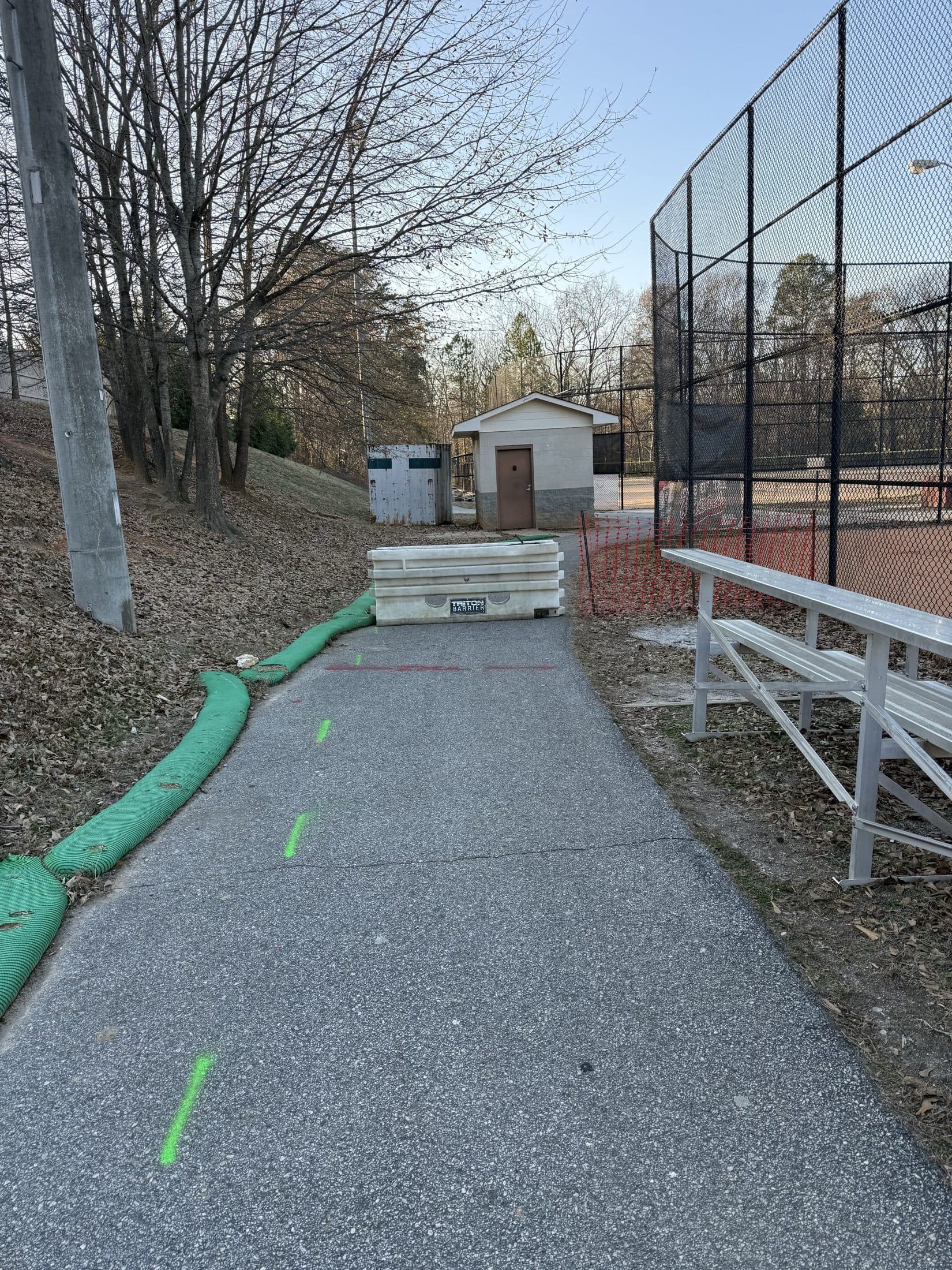 The restored asphalt trail with silt sock along its edge, running past the bleachers and backstop