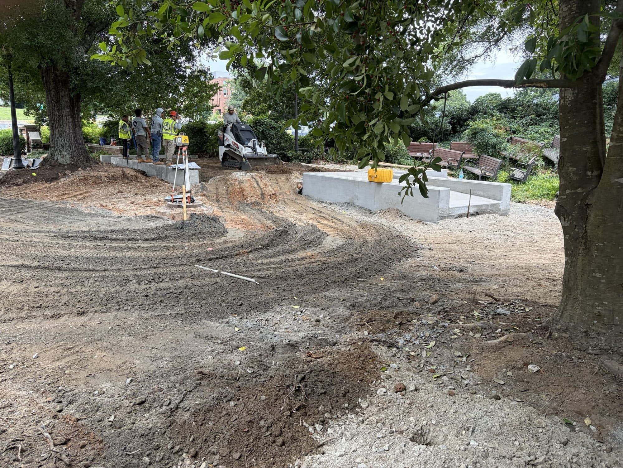 Survey instrument set up over the graded plaza subgrade with new concrete seat walls in place