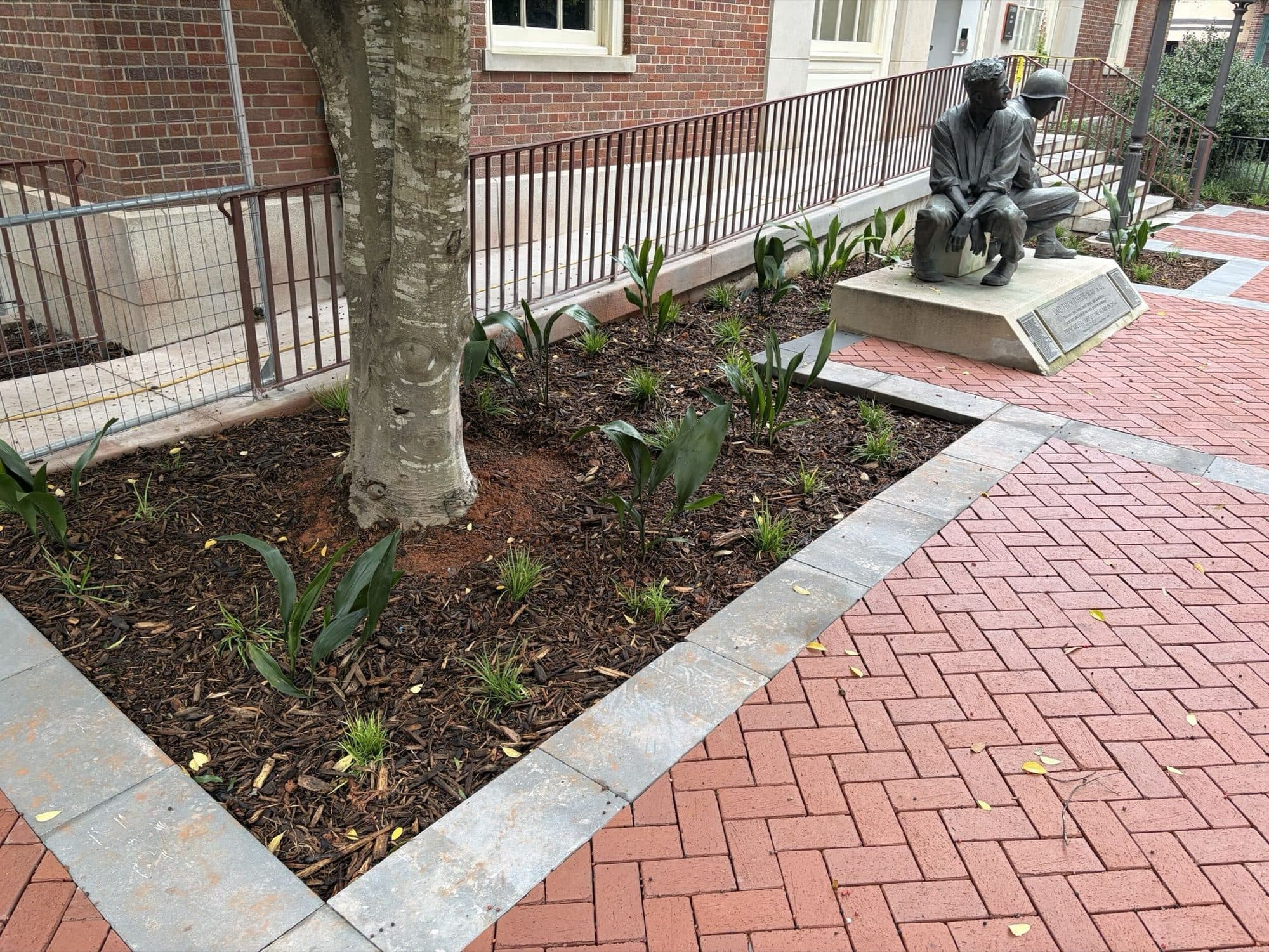 A bronze memorial and new plantings set into a bed within the finished brick plaza