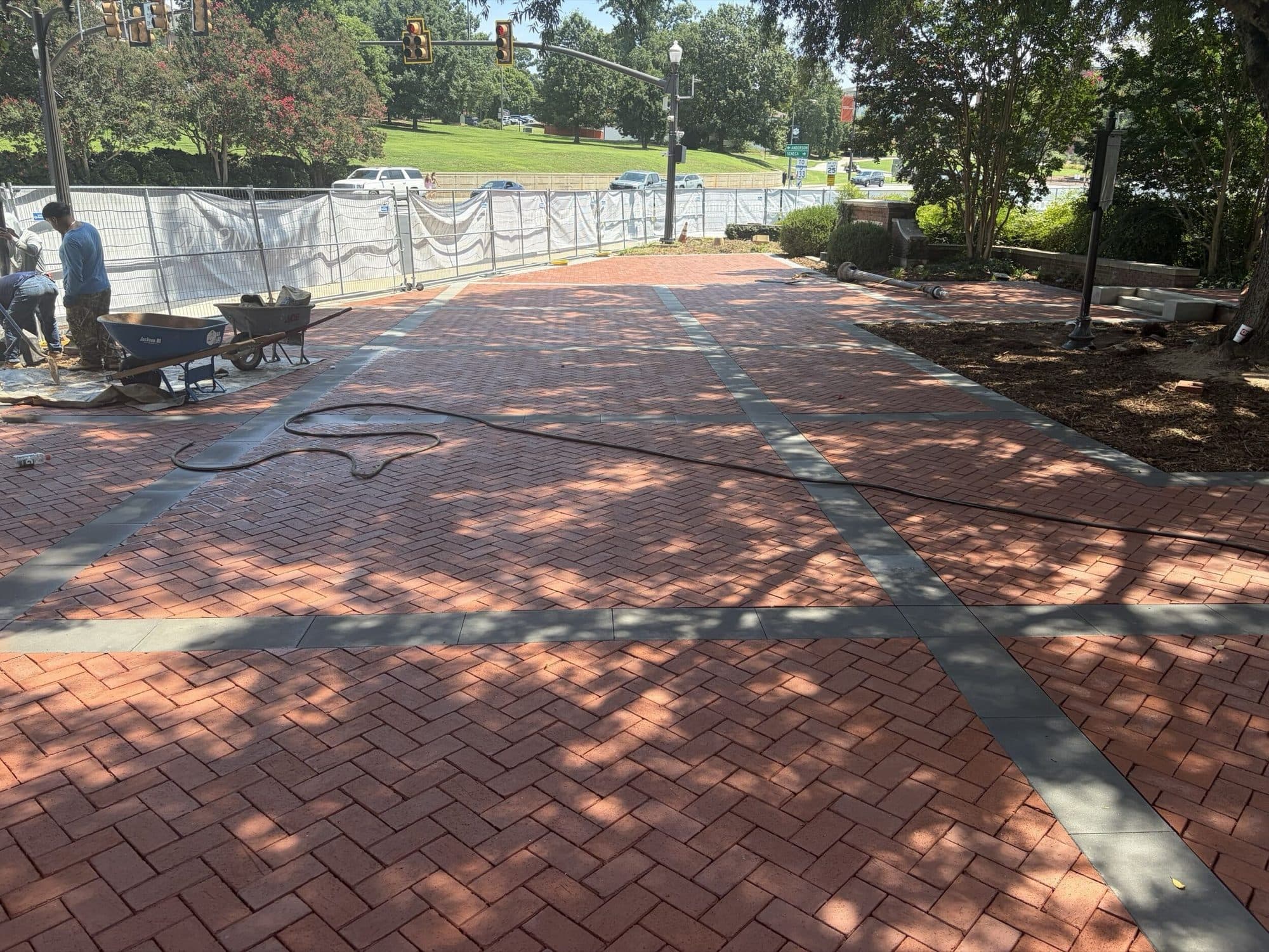 A mason setting clay pavers by hand across the plaza with wheelbarrows of material alongside