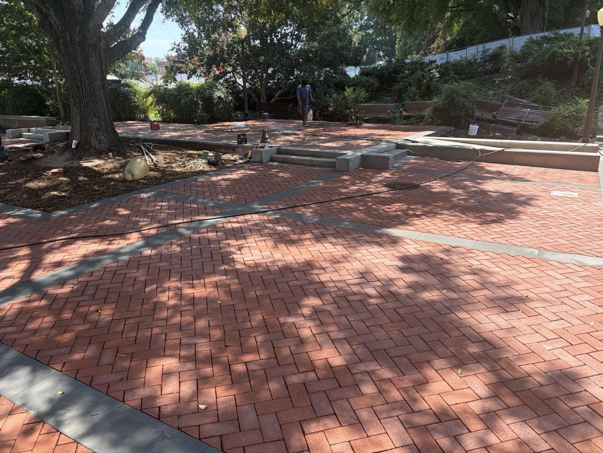 The same plaza area finished in clay pavers with concrete banding, benches, and planting beds