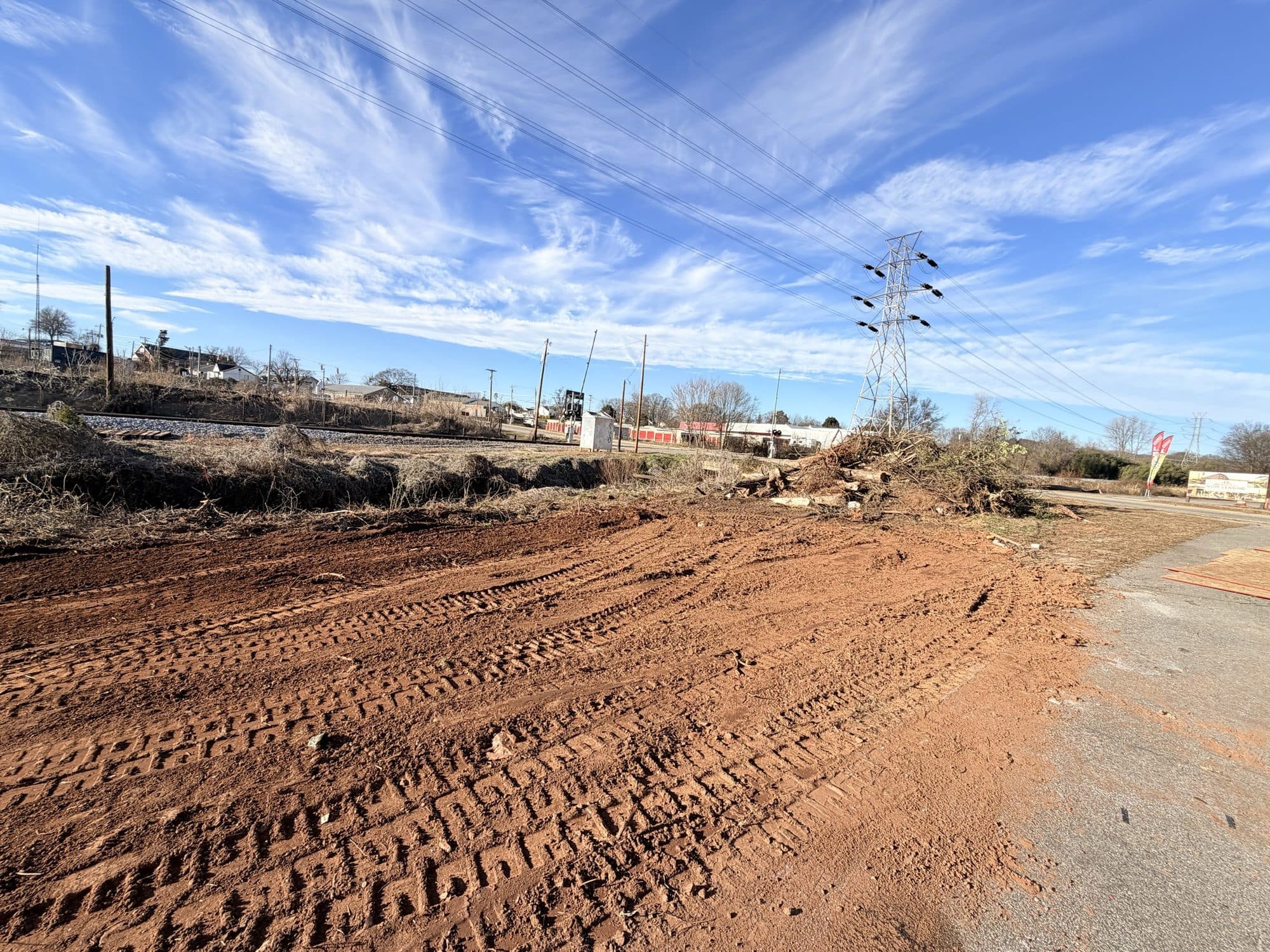 The corridor cleared and graded down to bare earth, with the rail line beyond