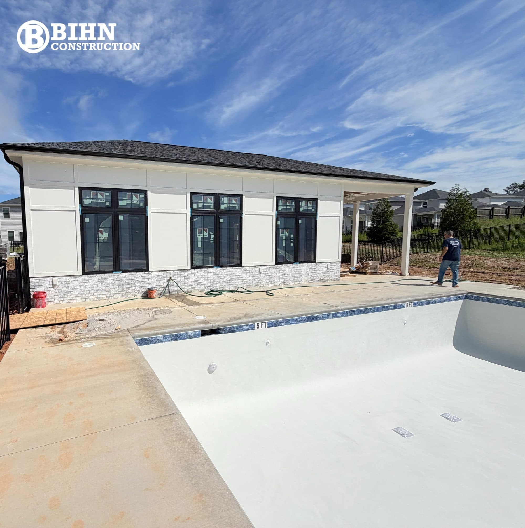 The completed Gramercy Woods clubhouse, board and batten over a stone base, with the finished pool and deck in front of it