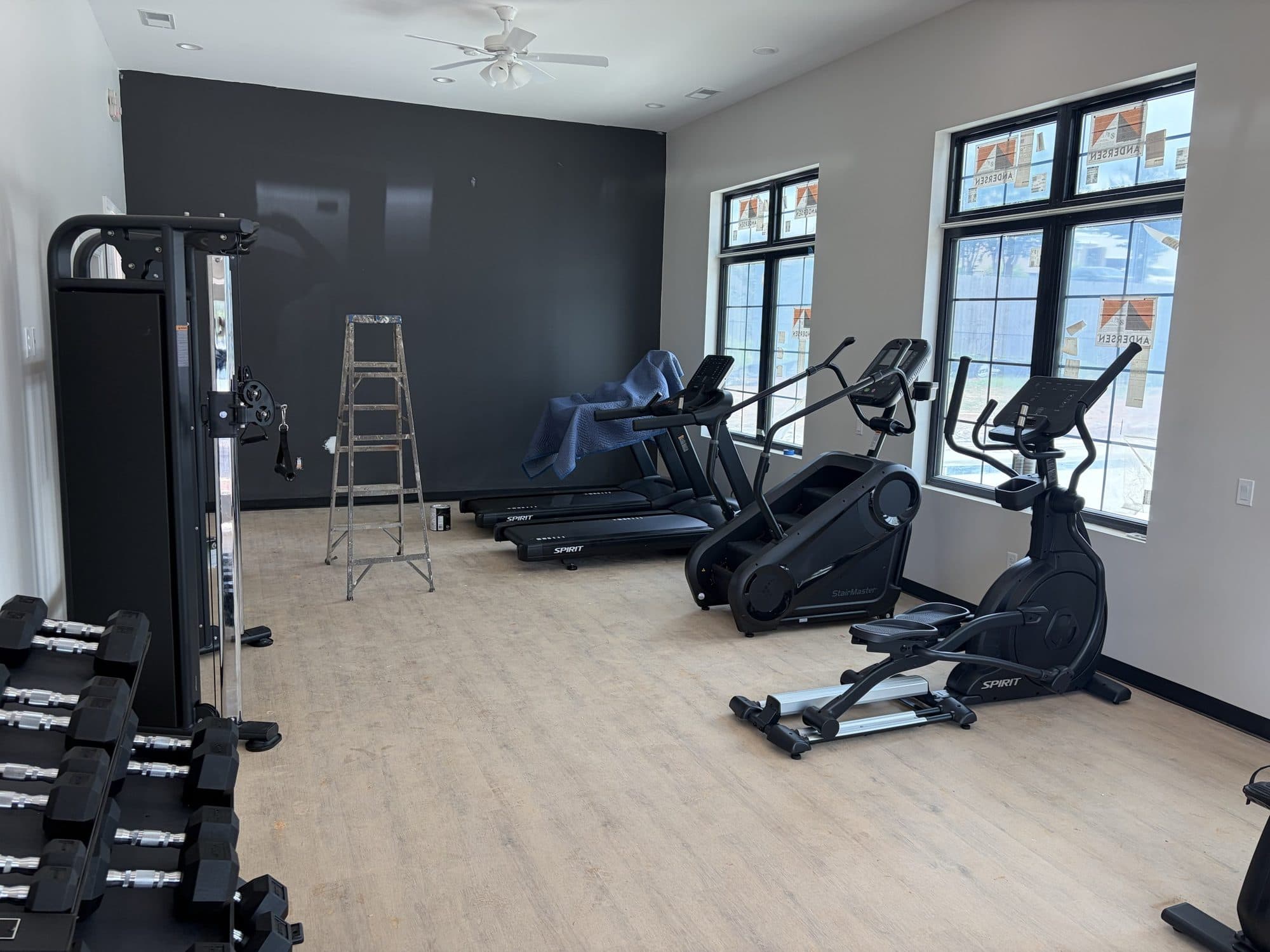 The fitness room's charcoal accent wall with cardio equipment and free weights set along the windows