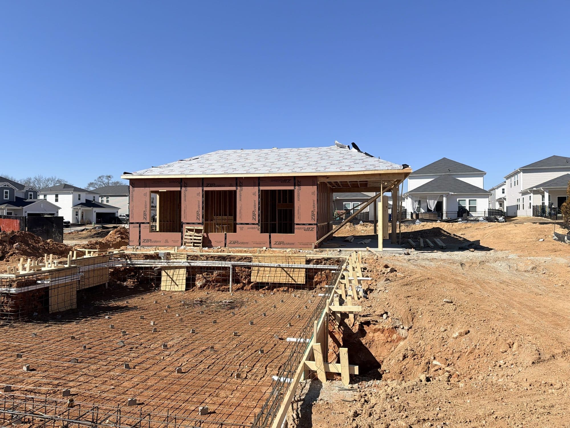 The clubhouse framed and roofed, sheathed and papered, with the pool area still at raw grade