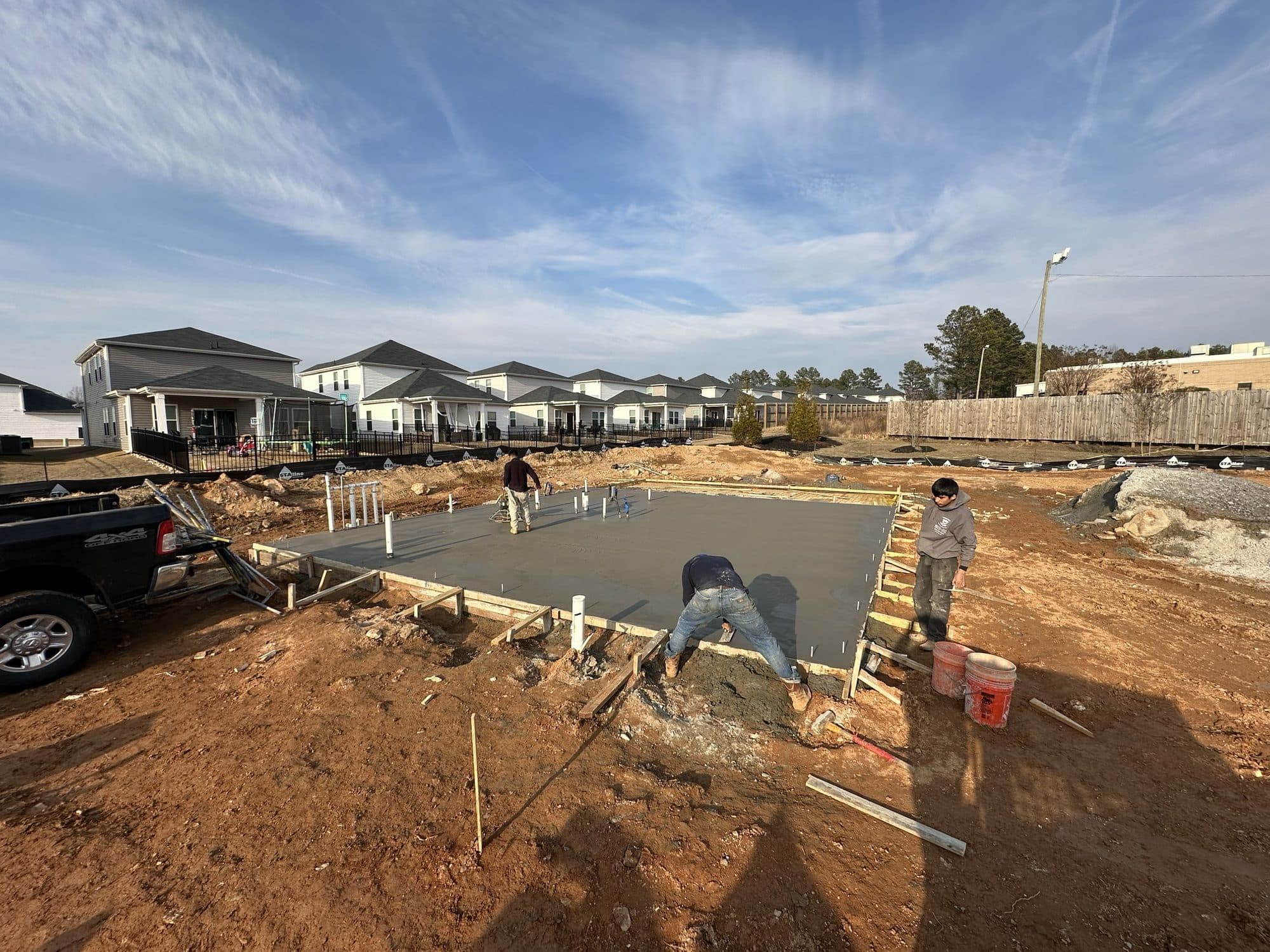 Crew finishing the concrete pool deck slab with the community homes in the background