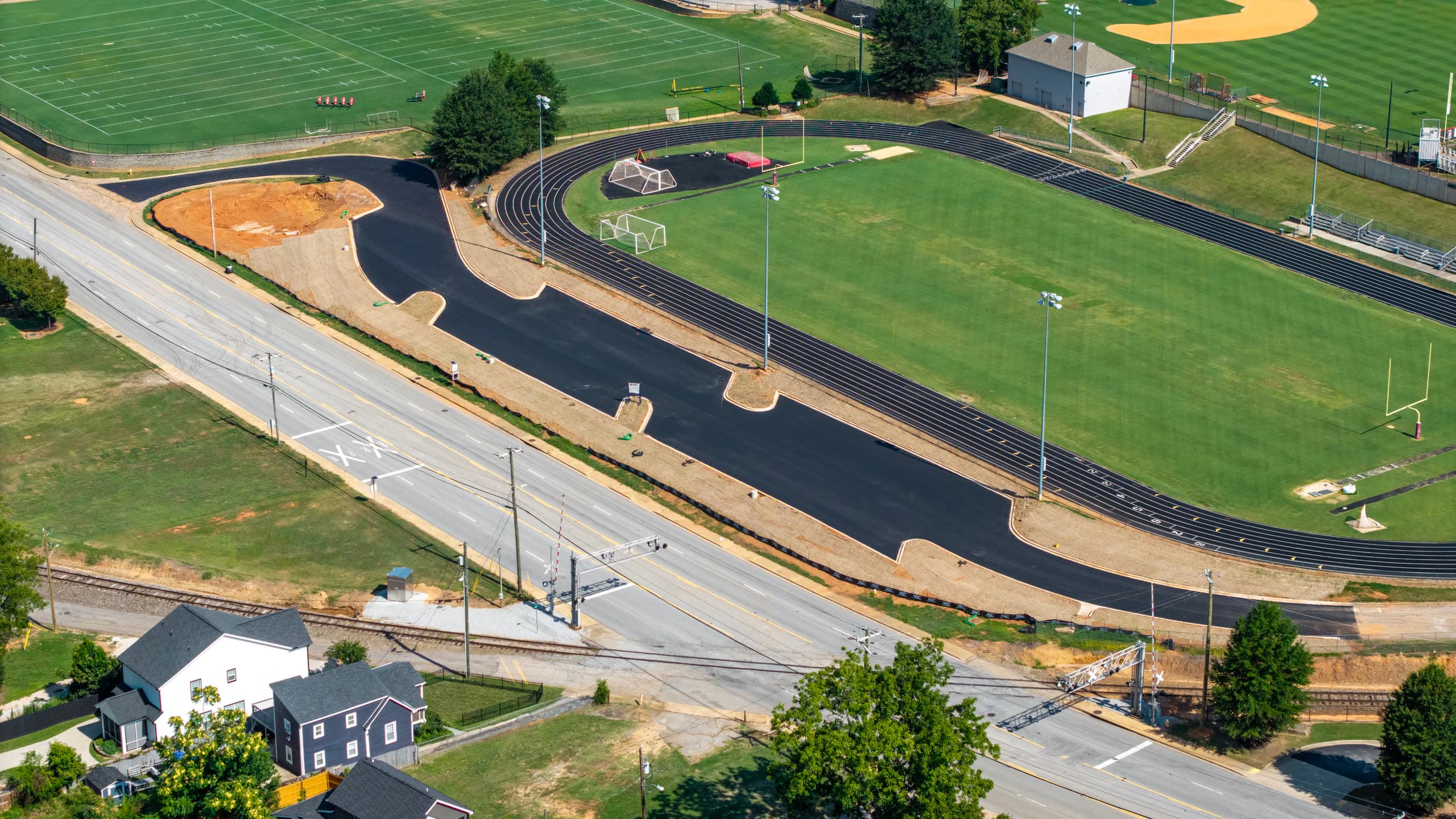 Aerial view of the newly paved Greenville High School parking lot running between the road and the track, with the rail crossing in the foreground