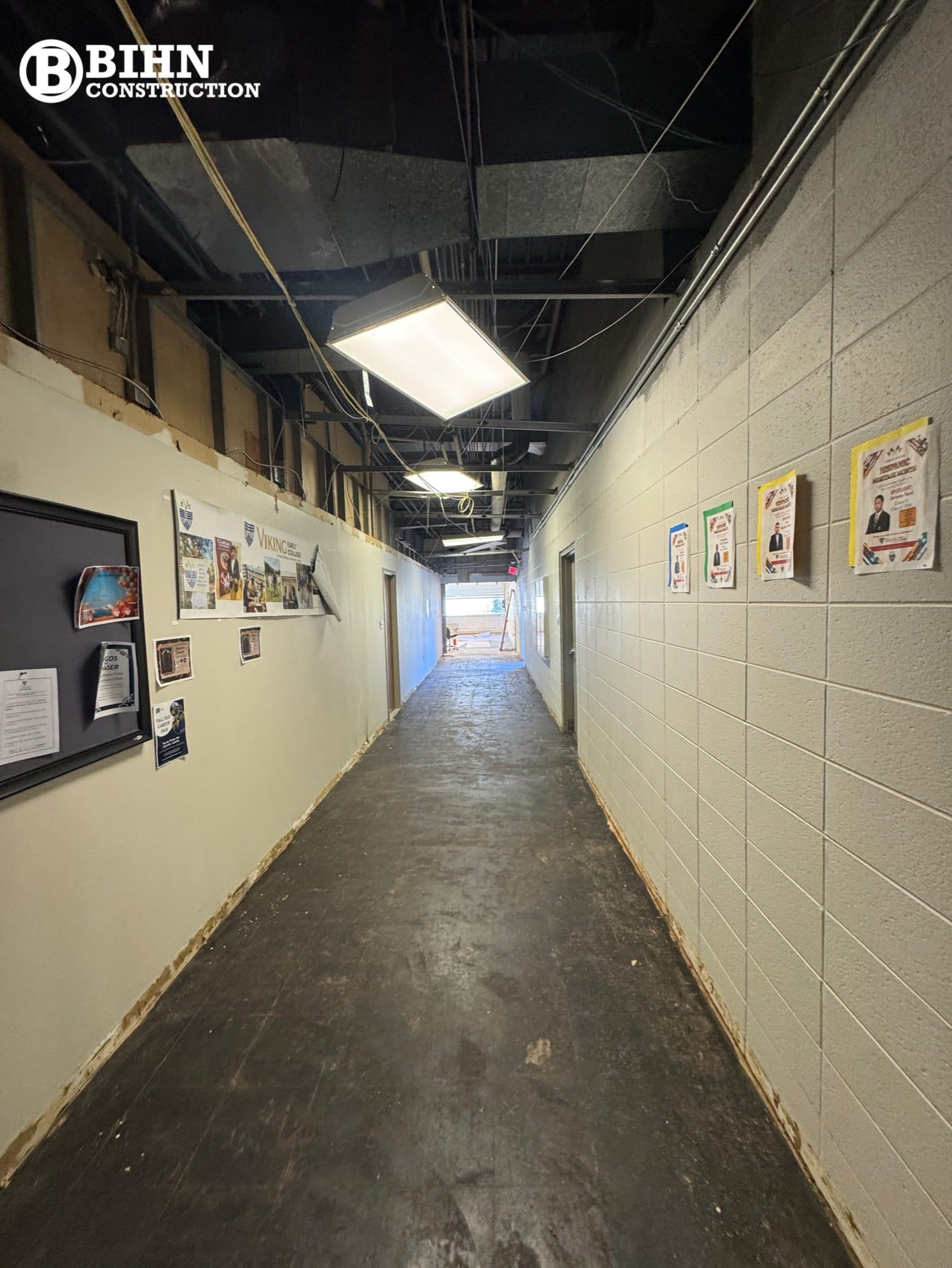 The corridor before the work, with the ceiling opened for demolition, exposed wiring, and worn flooring